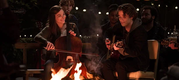 Livro e Filme Se Eu Ficar. A protagonista toca violoncelo entre seus familiares em frente a uma fogueira.